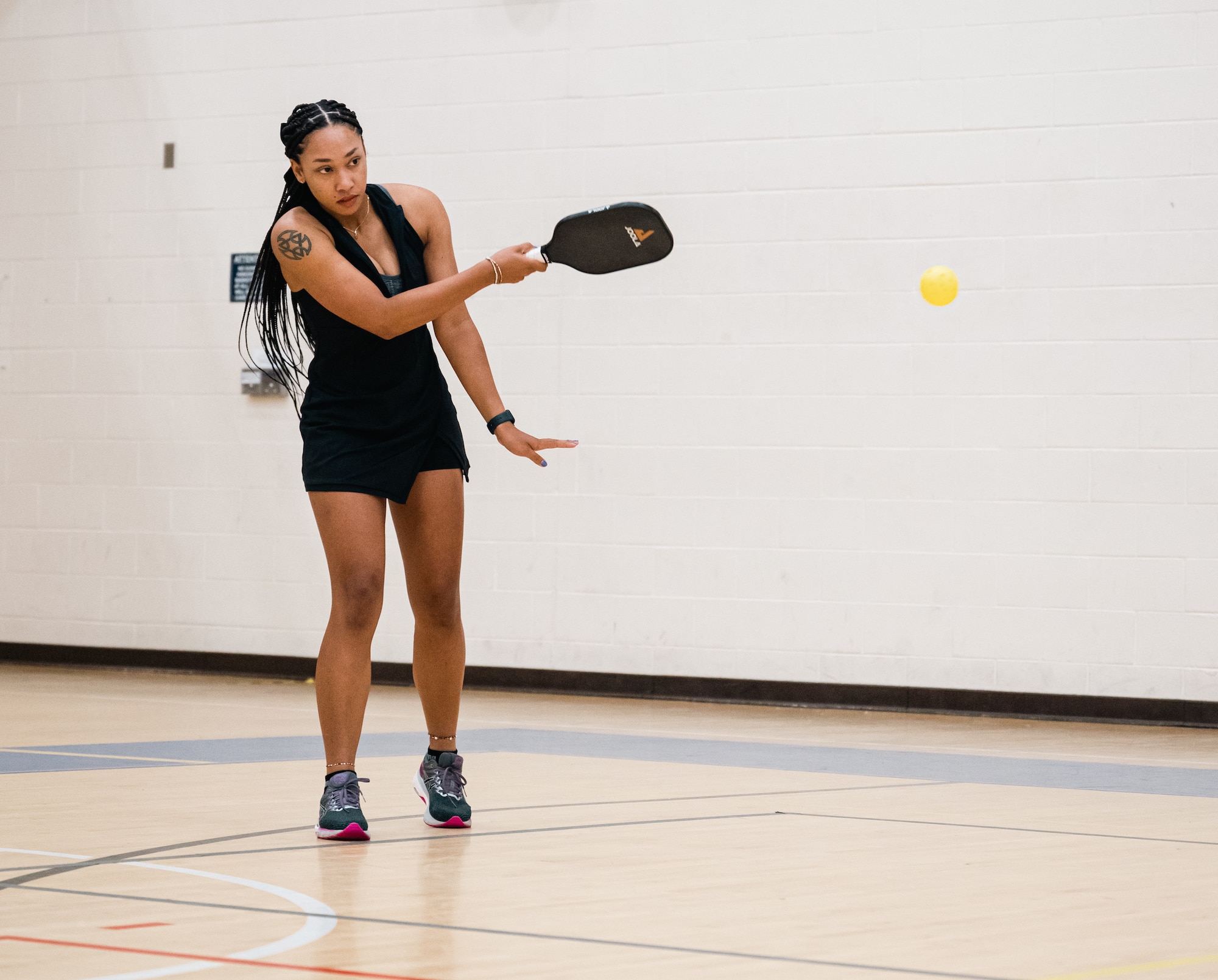 Woman with long black hair is looks like she is moving to hit a small ball with a black paddle.