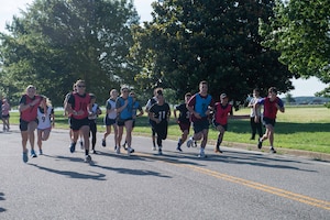 People running in a race on a road in a large group on a sunny day.