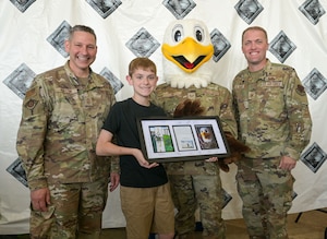Two uniformed service members pose with an eagle mascot and a child holding an award.