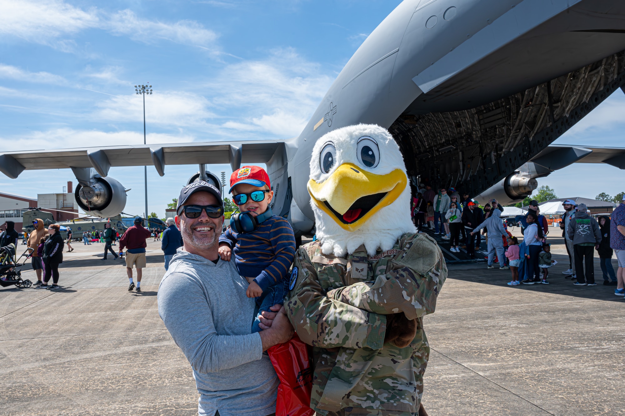 An eagle mascot poses with a father and a daughter in front of a large cargo plane display.