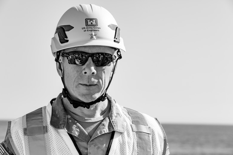Black and white image of a man in a helmet and safety vest with the ocean in the background