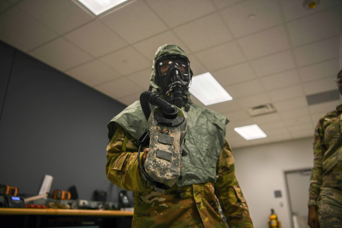 A service member demonstrates how to use a flight gas mask.