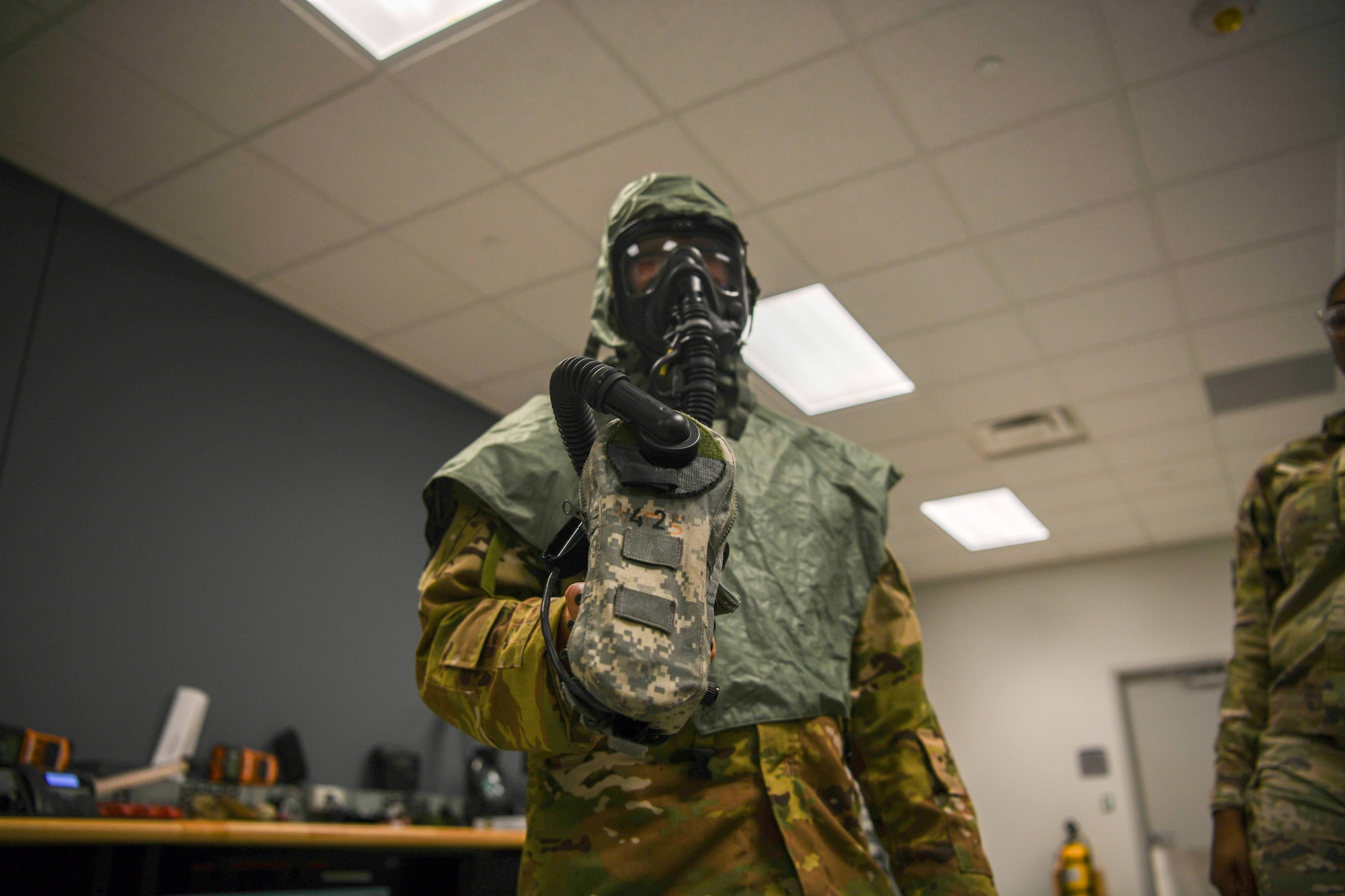 A service member demonstrates how to use a flight gas mask.