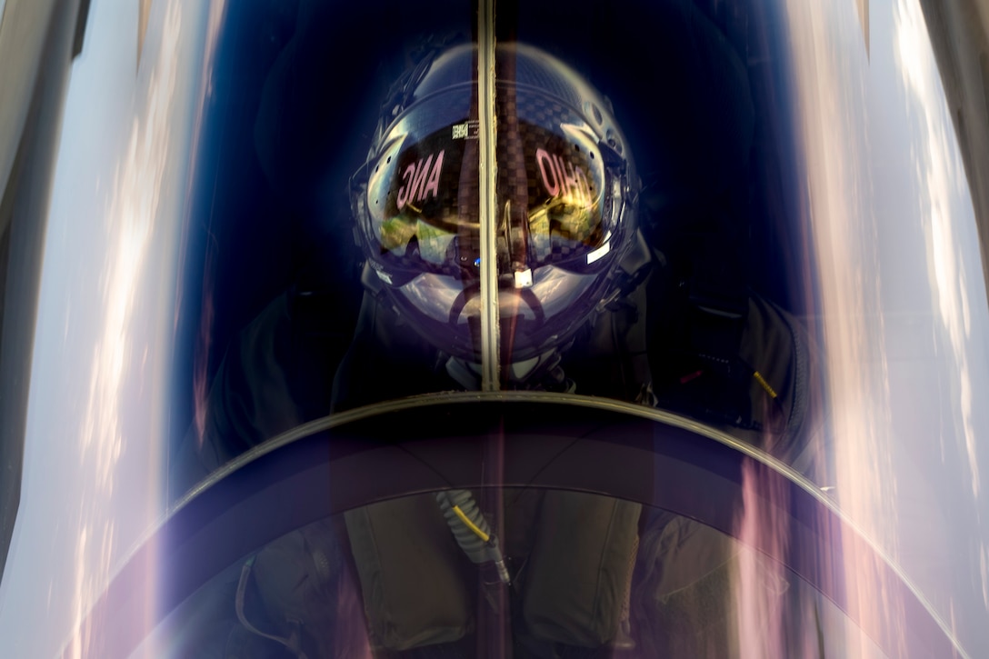 A pilot in a reflective helmet is seen close up from above in an aircraft.