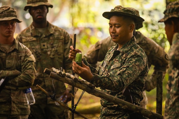 A Malaysian Army soldier demonstrates a traditional bamboo trap designed to catch small animals such as squirrels, highlighting indigenous survival techniques shared with Australian and U.S. Army partners during jungle training.