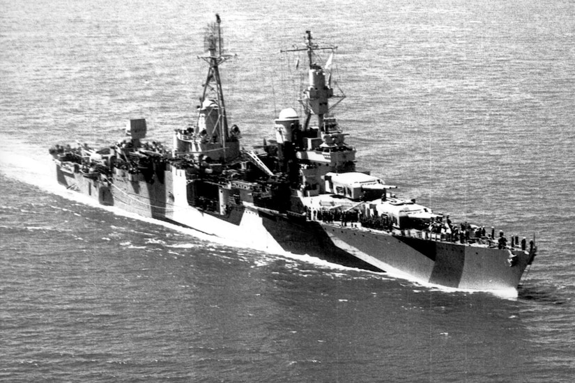 An aerial view of a military ship with big guns is sailing through the ocean.