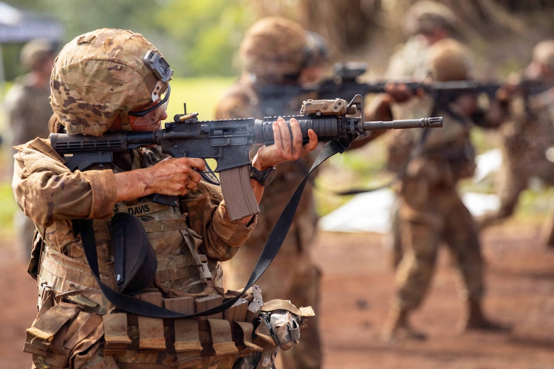 A soldier in tactical gear fires a service weapon to the right while other soldiers do the same in the background.