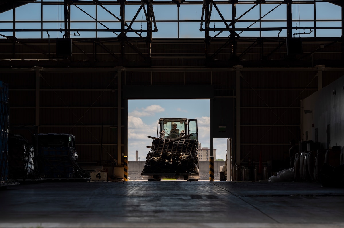 A military member drives a forklift through the entrance of a warehouse.