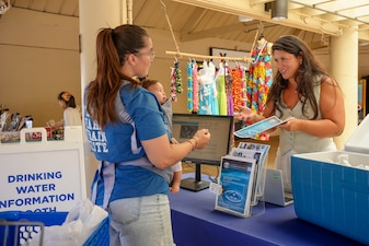 A Navy Closure Task Force-Red Hill (NCTF-RH) community liaison officer shares an information pamphlet at a drinking water information booth at the Hickam Exchange on Joint Base Pearl Harbor-Hickam, Hawaii, July 10, 2025. Monthly events like this help inform residents about drinking water testing and where they can search for results online. Charged with the safe decommissioning of the Red Hill Bulk Fuel Storage Facility, NCTF-RH was established by the Department of the Navy as a commitment to the community and the environment. NCTF-RH continues to engage with the people of Hawaii, regulatory agencies, and other stakeholders as it safely and deliberately decommissions the facility. (U.S. Navy photo by Mass Communication Specialist 3rd Class Krystal Diaz)