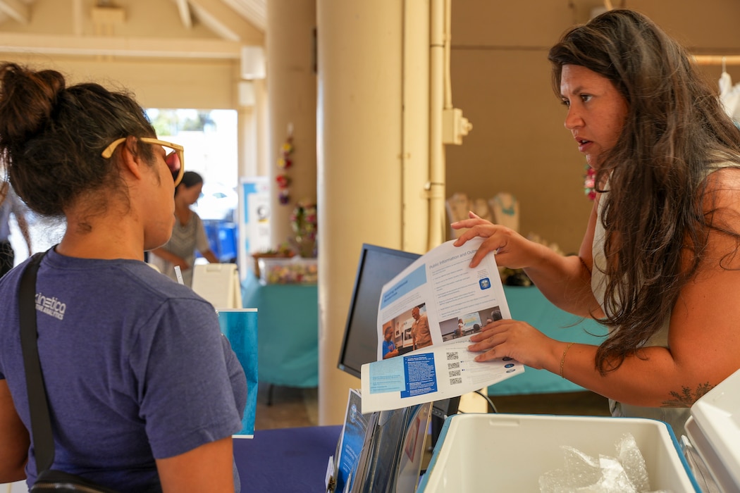 A Navy Closure Task Force-Red Hill (NCTF-RH) community liaison officer shares an information pamphlet during a drinking water information booth at the Hickam Exchange on Joint Base Pearl Harbor-Hickam, Hawaii, July 10, 2025. Monthly events like this help inform residents about drinking water testing and where they can search for results online. Charged with the safe decommissioning of the Red Hill Bulk Fuel Storage Facility, NCTF-RH was established by the Department of the Navy as a commitment to the community and the environment. NCTF-RH continues to engage with the people of Hawaii, regulatory agencies, and other stakeholders as it safely and deliberately decommissions the facility. (U.S. Navy photo by Mass Communication Specialist 3rd Class Krystal Diaz)