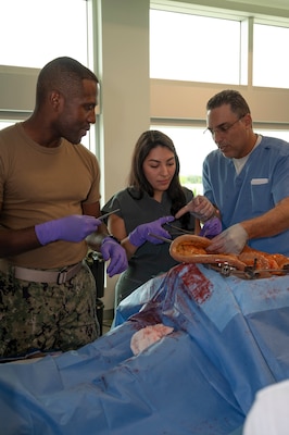 FORT LAUDERDALE, Fla. (July 12, 2025) Lt. Cmdr. Daniel Johnson, an orthopedic surgeon with Navy Medicine Readiness and Training Command Jacksonville, left, and Dr. Aeyal Oren, a general surgeon in private practice in Plantation, right, use a Tactical Combat Casualty Care Cut Suit to demonstrate emergency abdominal surgery to a participant during the “Top Doc” event at Nova Southeastern University’s Fort Lauderdale campus. Navy Medicine and Navy Recruiting Command partnered with NSU to launch “Top Doc”, a national initiative connecting local medical professionals, educators, and students while highlighting Navy Medicine’s capabilities and career opportunities. (U.S. Navy Photo by Mass Communication Specialist 1st Class Natalia Murillo)