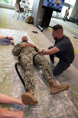 FORT LAUDERDALE, Fla. (July 12, 2025) Hospital Corpsman 2nd Class Jacob Munoz, assigned to Expeditionary Medical Facility 150-Mike, Navy Medicine Readiness and Training Command Jacksonville, guides a participant in applying a tourniquet during the "Top Doc" event at Nova Southeastern University's Fort Lauderdale campus. Navy Medicine and Navy Recruiting Command partnered  with NSU to launch “Top Doc”, a national initiative connecting local medical professionals, educators, and students while highlighting Navy Medicine’s capabilities and career opportunities. (U.S. Navy Photo by Mass Communication Specialist 1st Class Natalia Murillo)