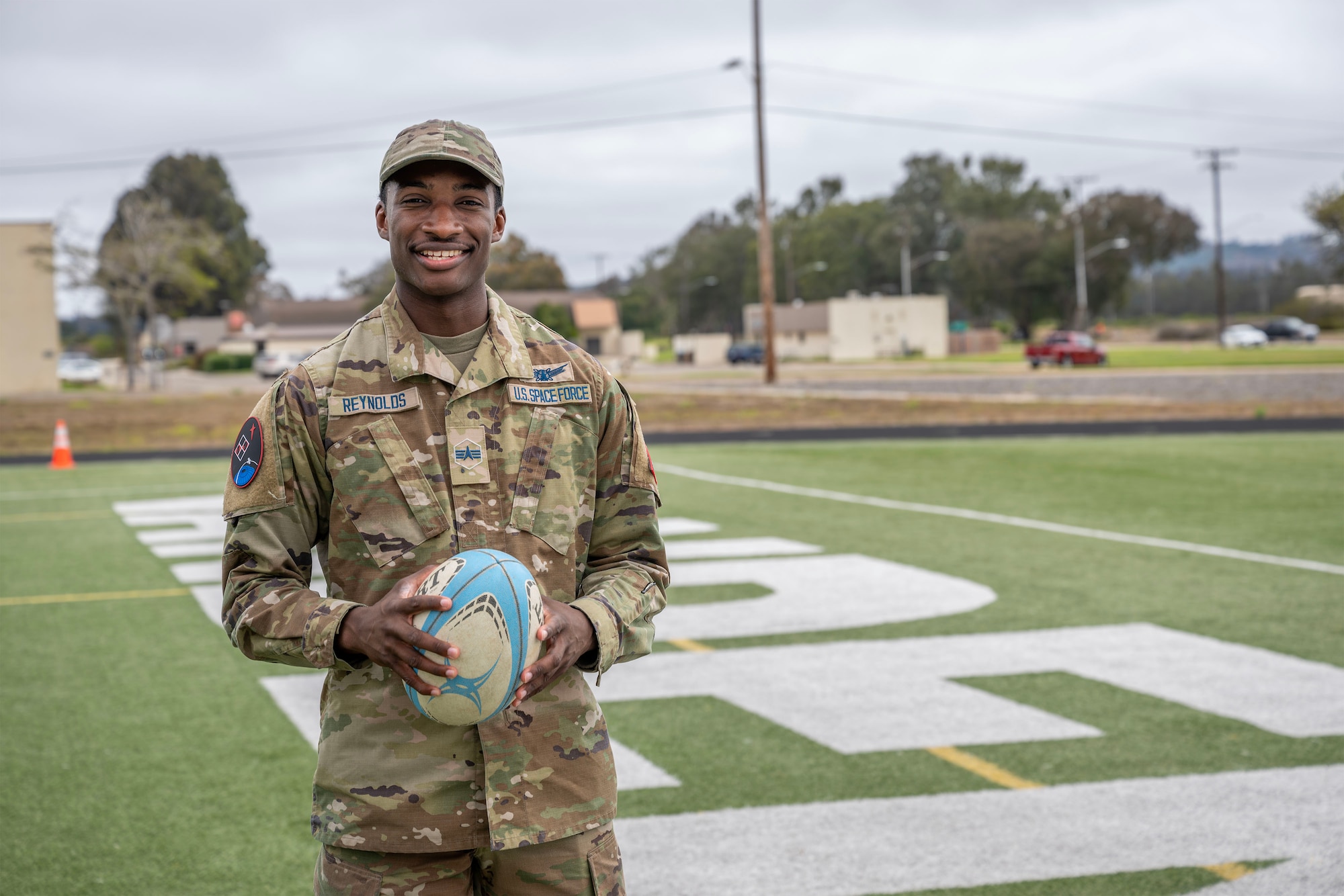 A Space Force solider poses with a rugby ball.