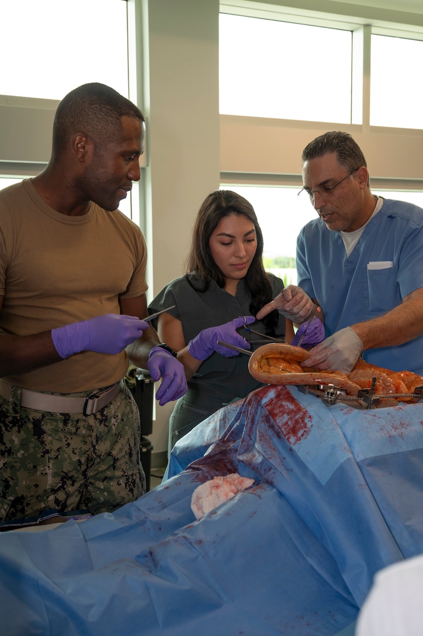 FORT LAUDERDALE, Fla. (July 12, 2025) Lt. Cmdr. Daniel Johnson, an orthopedic surgeon with Navy Medicine Readiness and Training Command Jacksonville, left, and Dr. Aeyal Oren, a general surgeon in private practice in Plantation, right, use a Tactical Combat Casualty Care Cut Suit to demonstrate emergency abdominal surgery to a participant during the “Top Doc” event at Nova Southeastern University’s Fort Lauderdale campus. Navy Medicine and Navy Recruiting Command partnered with NSU to launch “Top Doc”, a national initiative connecting local medical professionals, educators, and students while highlighting Navy Medicine’s capabilities and career opportunities. (U.S. Navy Photo by Mass Communication Specialist 1st Class Natalia Murillo)