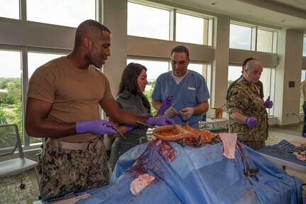 FORT LAUDERDALE, Fla. (July 12, 2025) Lt. Cmdr. Daniel Johnson, an orthopedic surgeon with Navy Medicine Readiness and Training Command Jacksonville, left, and Dr. Aeyal Oren, a general surgeon in private practice in Plantation, right, use a Tactical Combat Casualty Care Cut Suit to demonstrate emergency abdominal surgery to a participant during the “Top Doc” event at Nova Southeastern University’s Fort Lauderdale campus. Navy Medicine and Navy Recruiting Command partnered with NSU to launch “Top Doc”, a national initiative connecting local medical professionals, educators, and students while highlighting Navy Medicine’s capabilities and career opportunities. (U.S. Navy Photo by Mass Communication Specialist 1st Class Natalia Murillo)