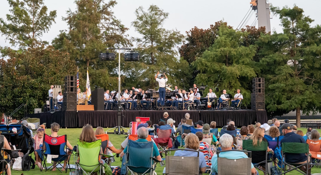 A crowd of people on a grassy field watch a band play music.