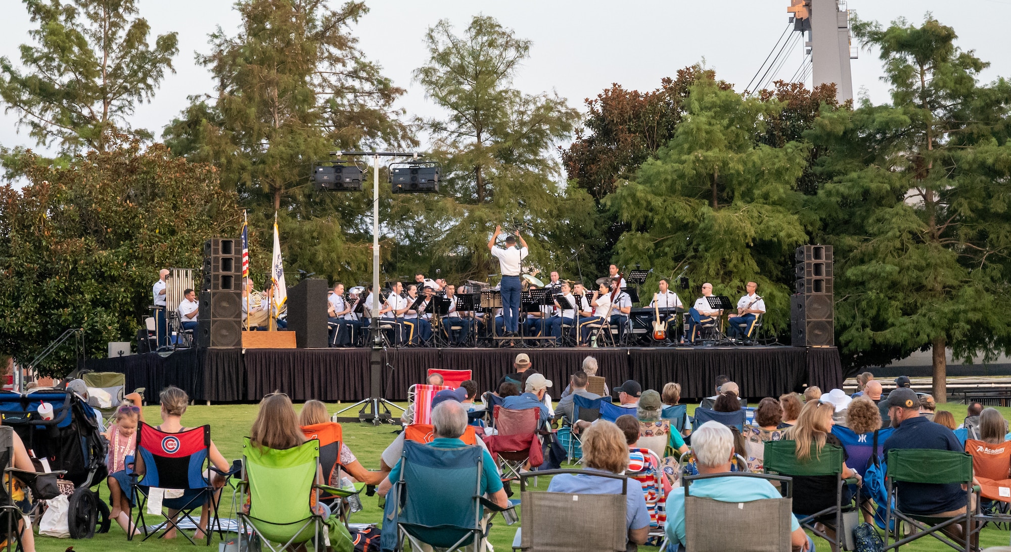 A crowd of people on a grassy field watch a band play music.