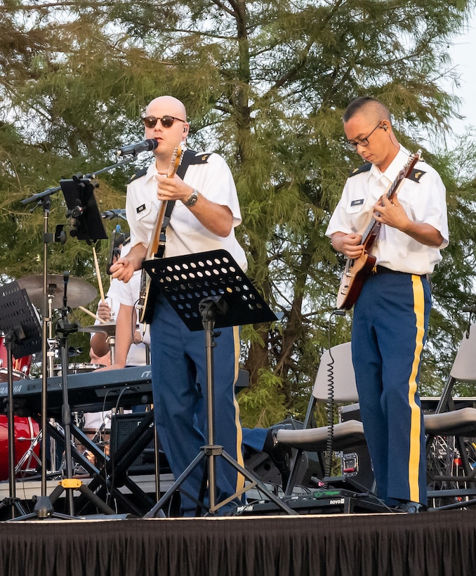 Two uniformed service members in blues play stringed instruments on a stage.