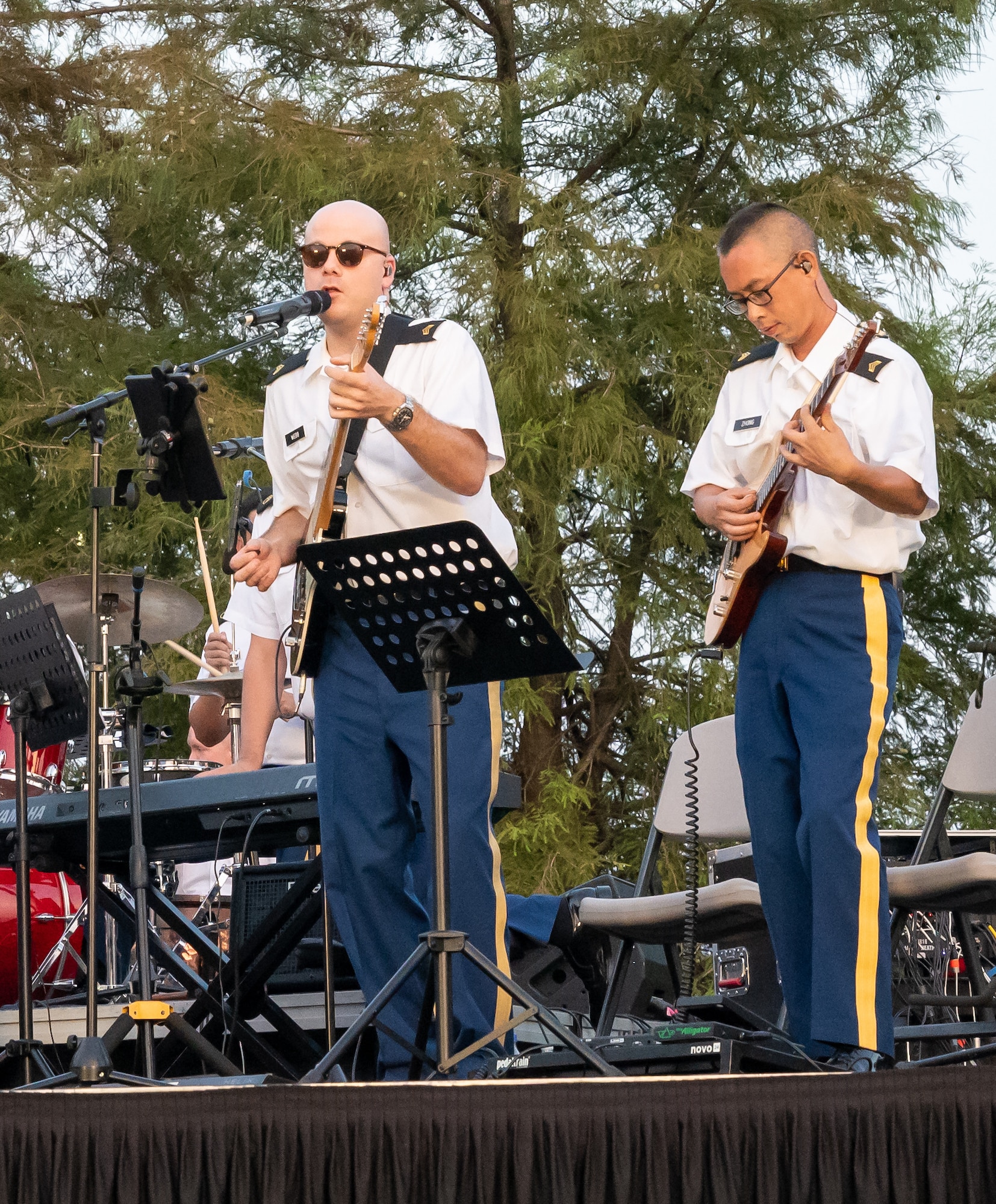 Two uniformed service members in blues play stringed instruments on a stage.