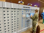 Service member holds a brown paper bag next to ScriptCenter automated machine.