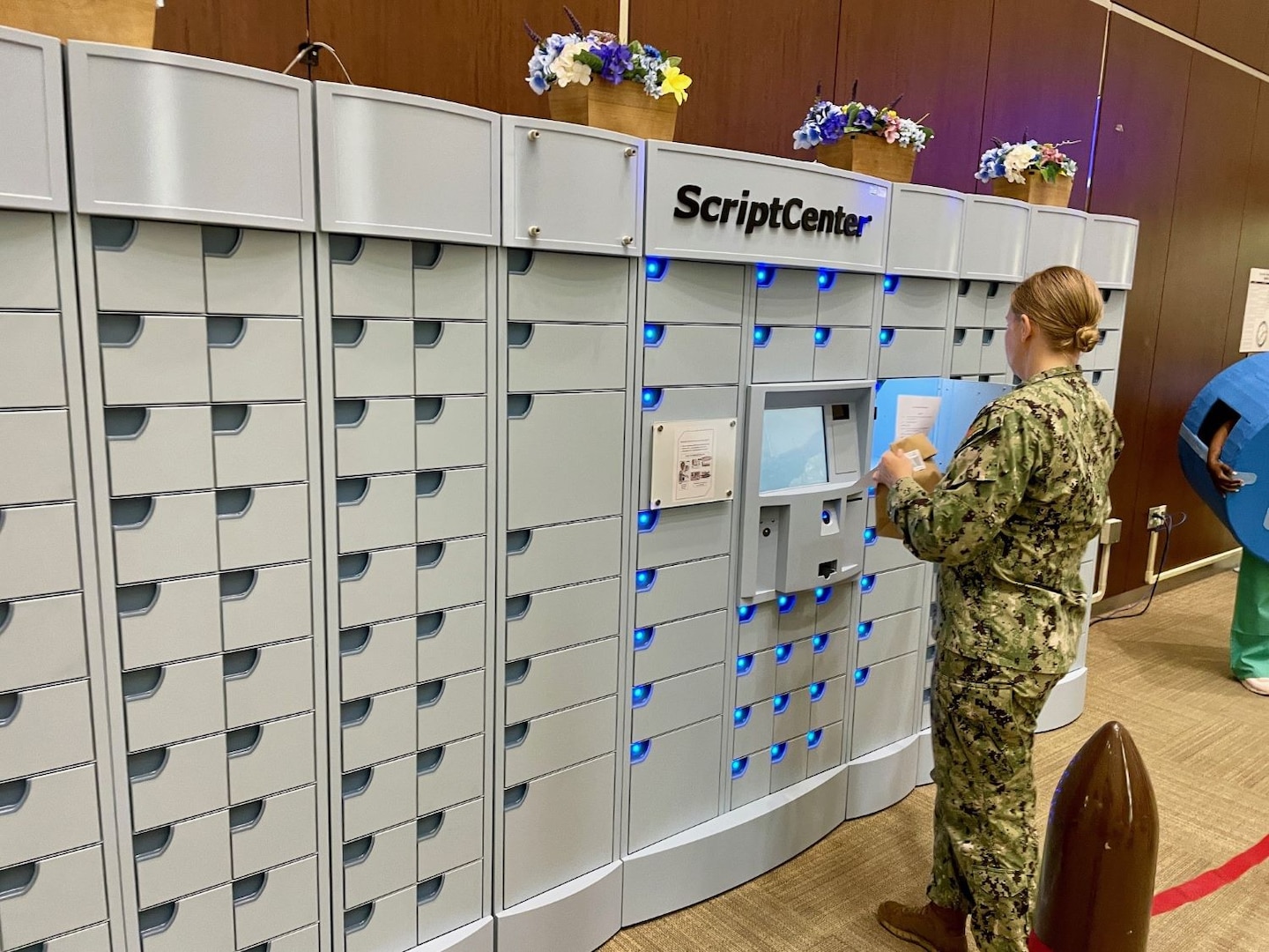 Service member holds a brown paper bag next to ScriptCenter automated machine.