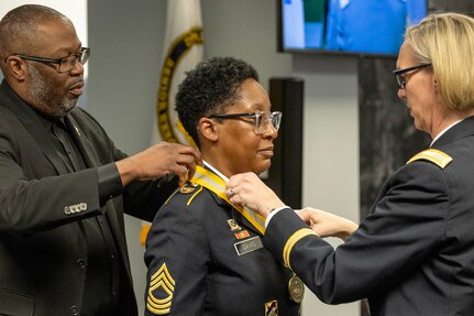 Col. Michelle M. Williams, U.S. Army Financial Management Command commander, right, and Retired Command Sgt. Maj. Gennaro Penn, U.S. Army Finance Corps Association president, left, present Master Sgt. Candace M. Davis, USAFMCOM Operational Support Team senior financial management systems instructor, with a Maj. Gen. Nathan Towson Regimental Medallion at the Maj. Gen. Emmett J. Bean Federal Center April 11, 2025. A native of Augusta, Georgia, Davis enlisted in the Army as a financial management specialist in October 2002. (U.S. Army photo by Mark R. W. Orders-Woempner)