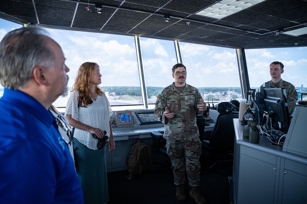 Two civilians and two military members can be seen in front of large windows