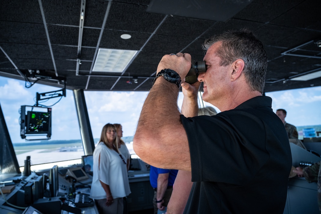 A man in a black polo has a pair of binoculars to his face