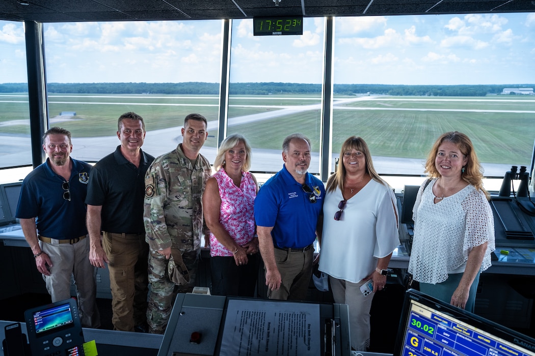 A seven-person group photo with a view of a flight line in the background
