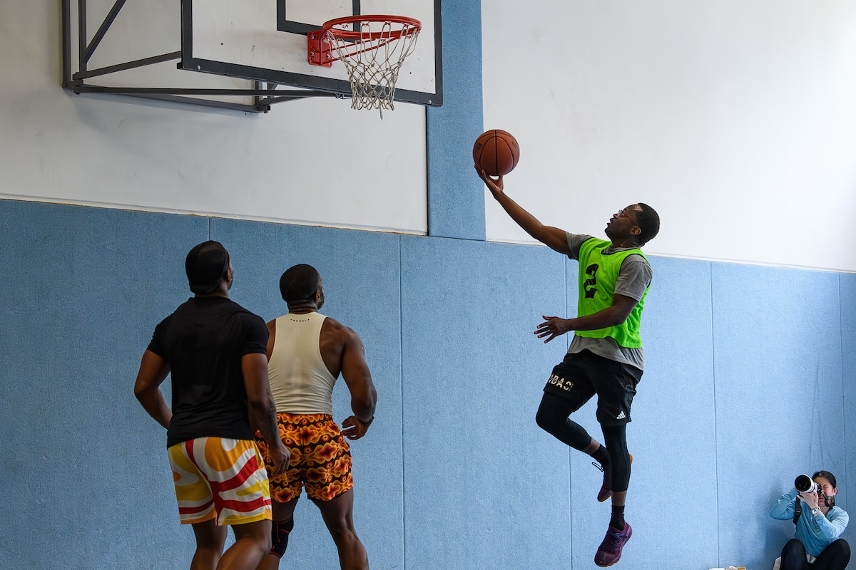 A man lays up a basketball as two other players watch.