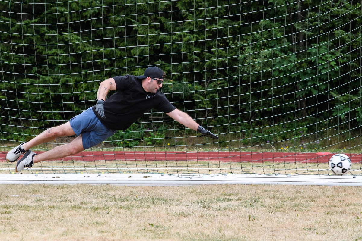 A soccer goalies dives as a ball goes past him into the net.