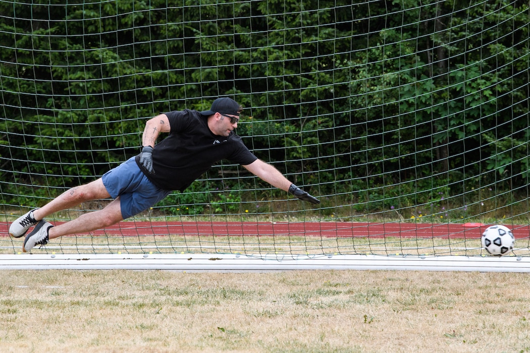 A soccer goalies dives as a ball goes past him into the net.