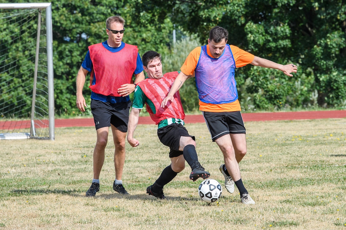 Two men try to kick a soccer ball while another man behind them runs towards them.