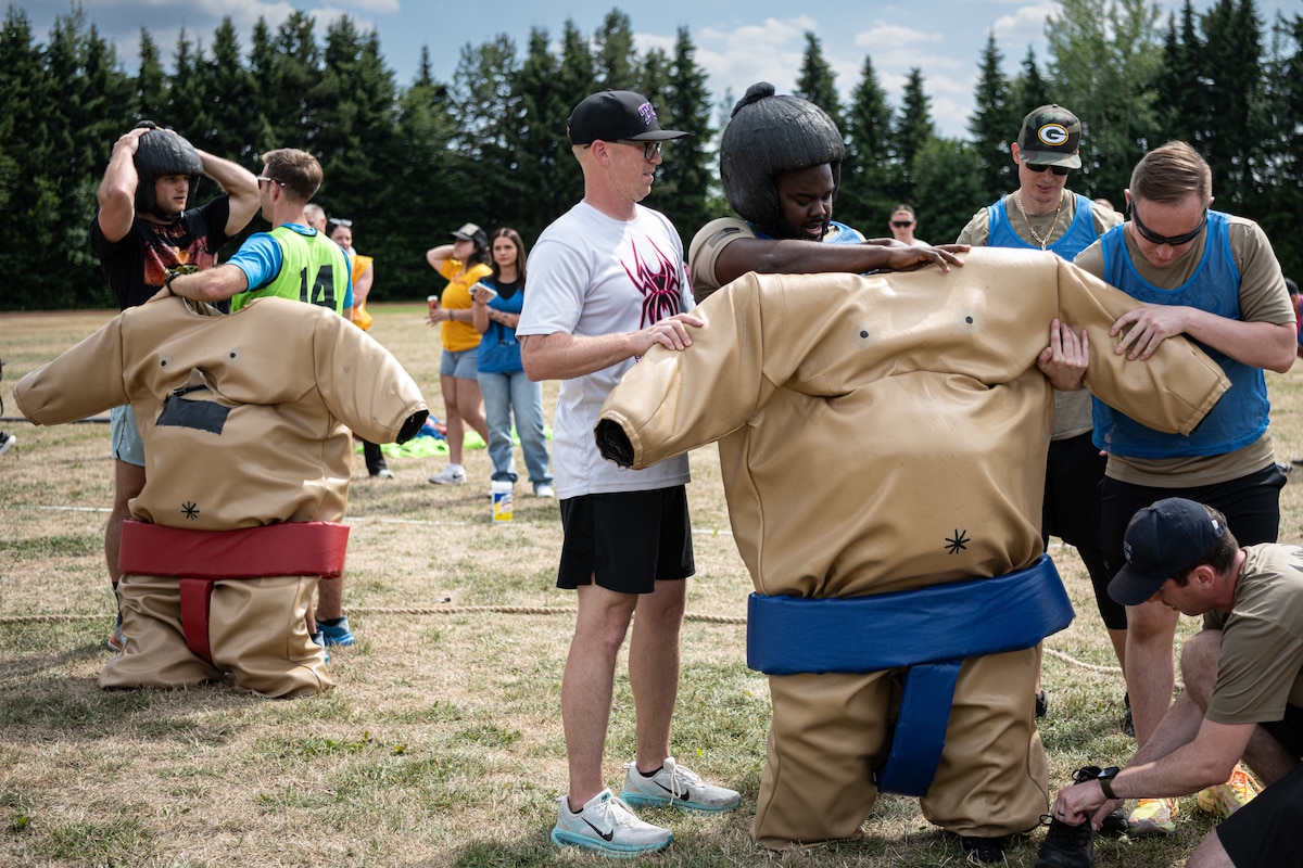 People help men into padded sumo suits.