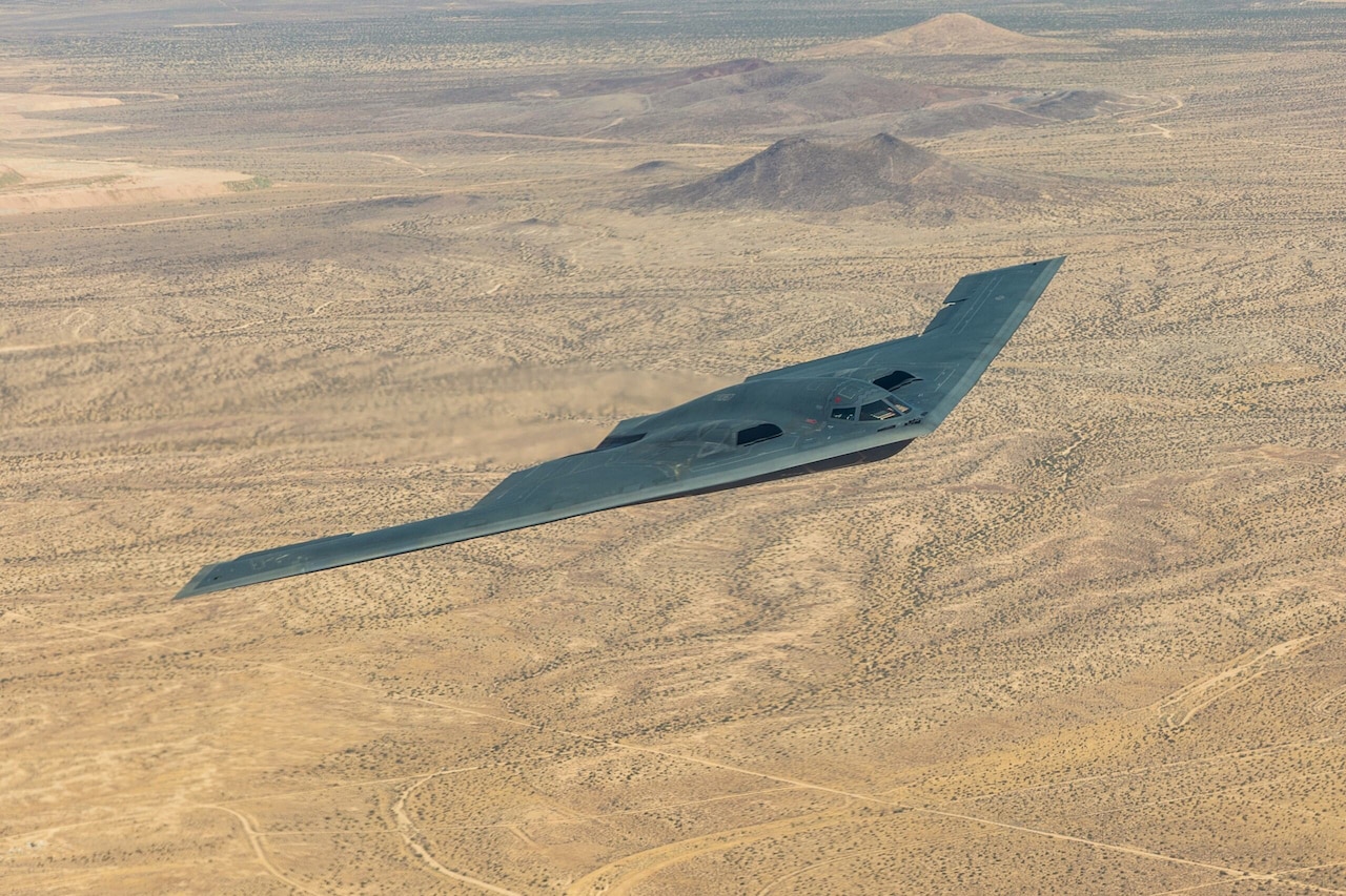 A triangular-shaped jet soars over a brown desert.