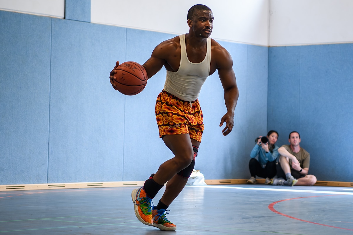 A basketball player dribbels a basketbal up a court.