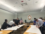 men and women cut paper patterns around a conference table