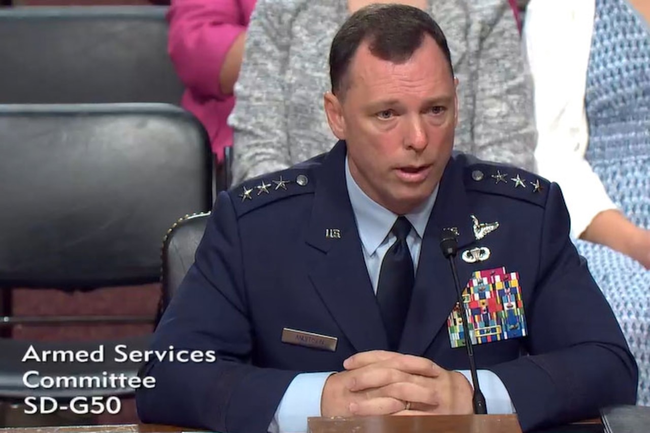 A man wearing a formal military uniform talks while seated behind a large wooden desk.