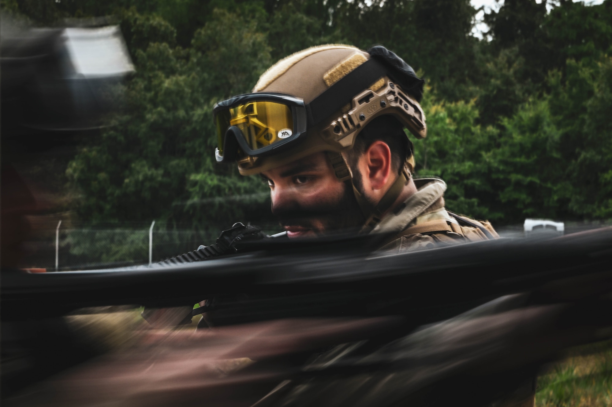 A man in uniform holding a rifle prepares to enter a building.