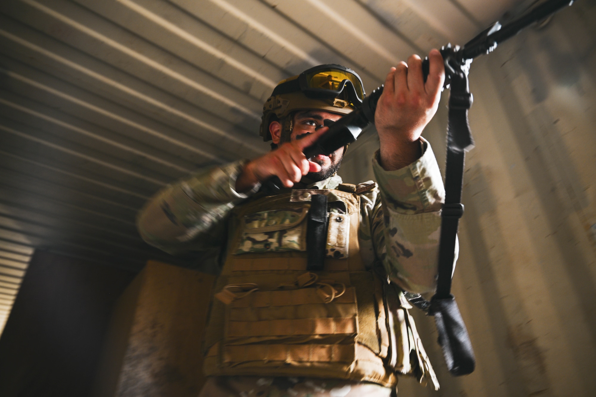 A man in uniform moves through a building with a rifle.