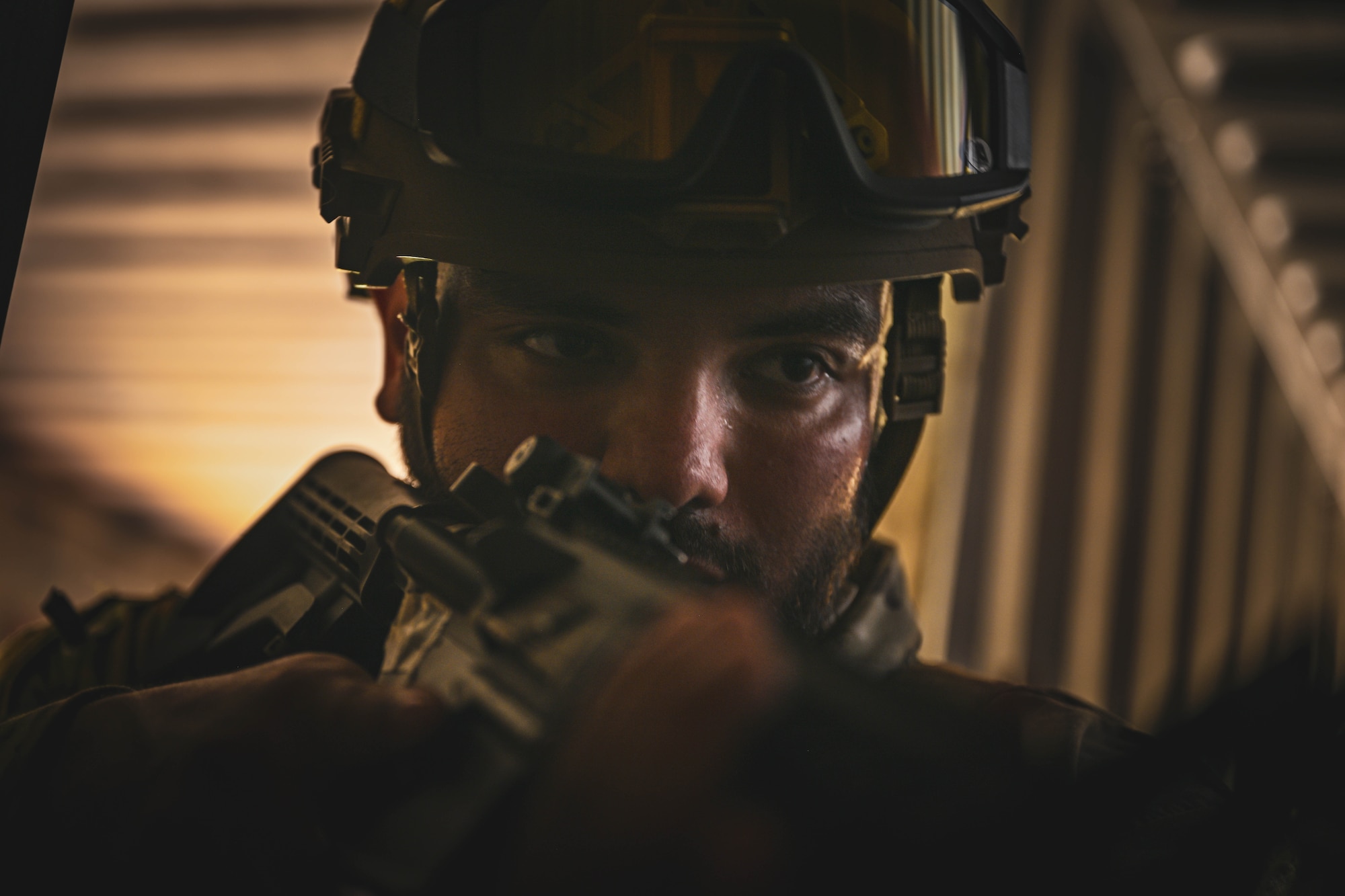 A man in uniform moves through a room with a rifle.