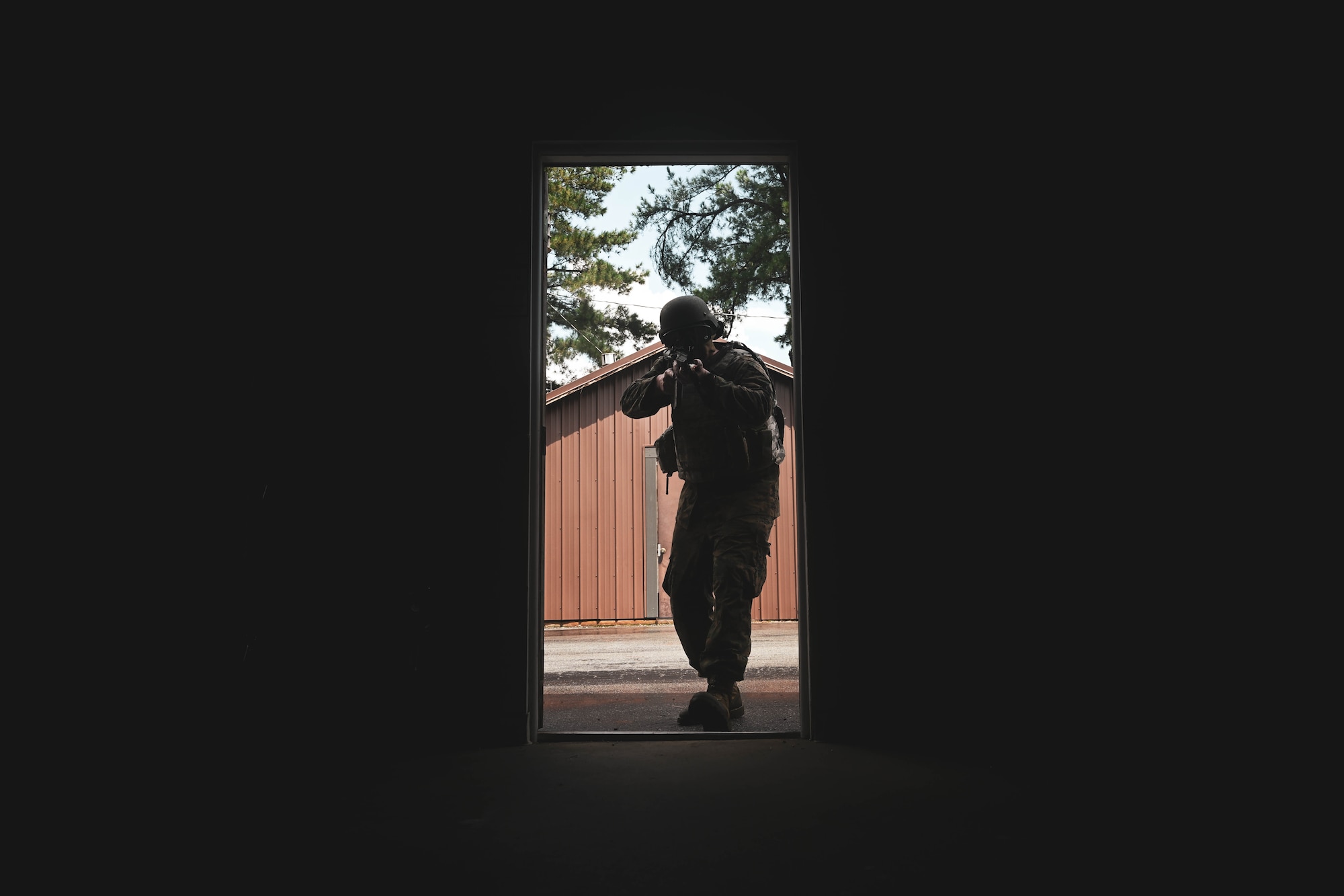 A man in uniform walks through a doorway holding a weapon.