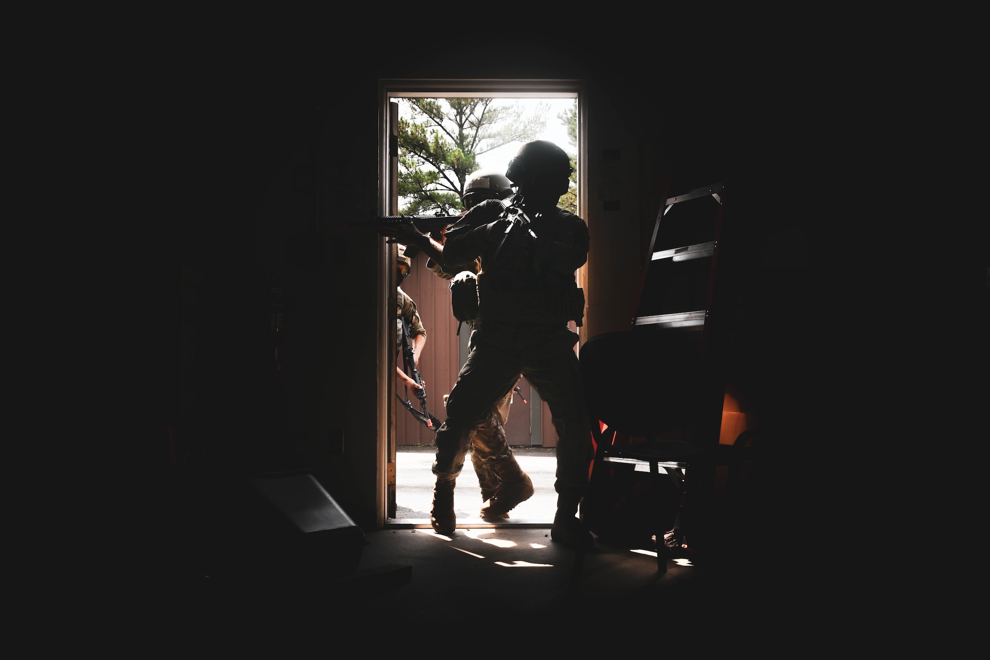 Men in uniform holding weapons charge through a doorway.
