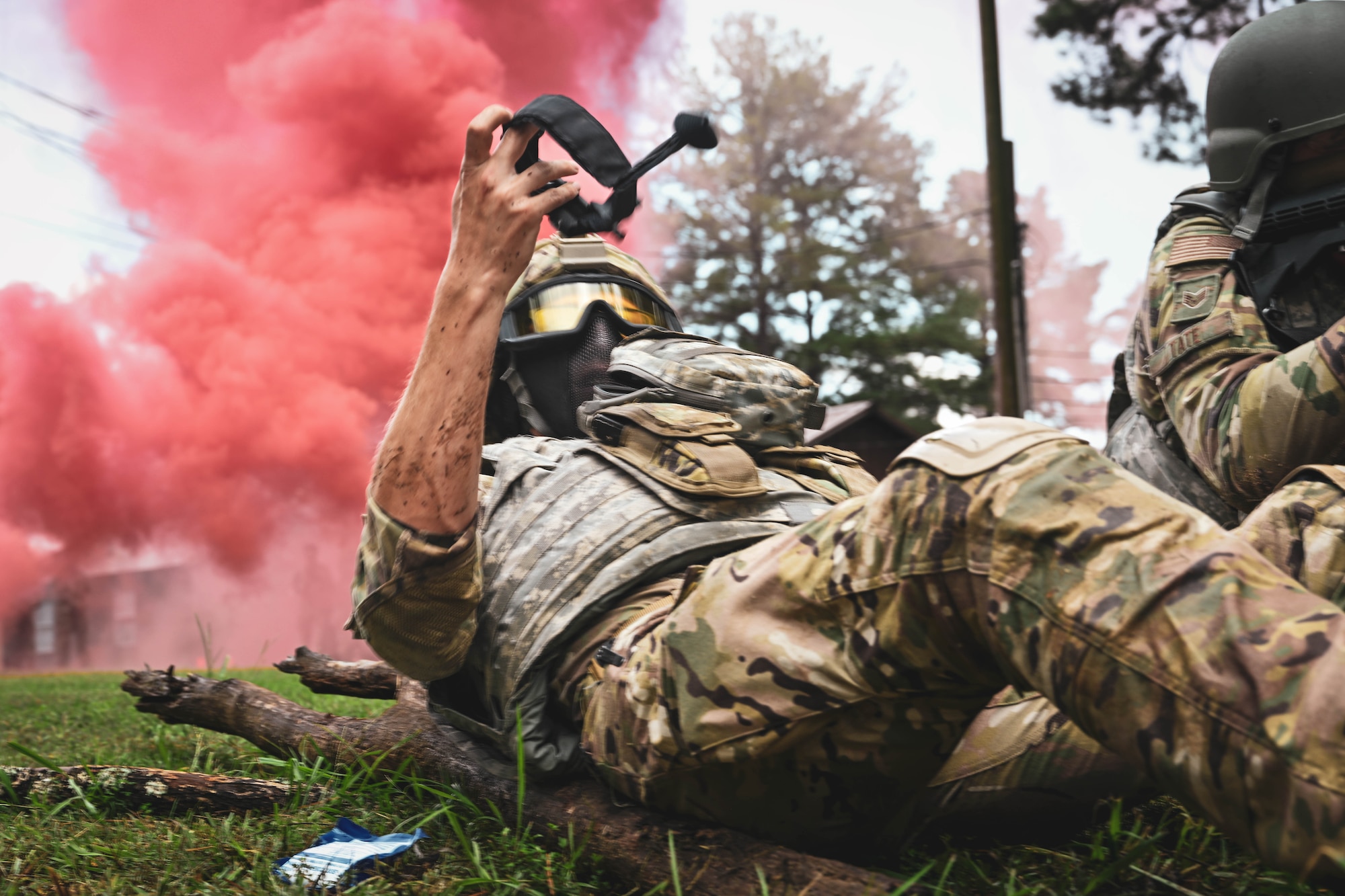 A man in uniform unfurls a tourniquet while lying on the ground.