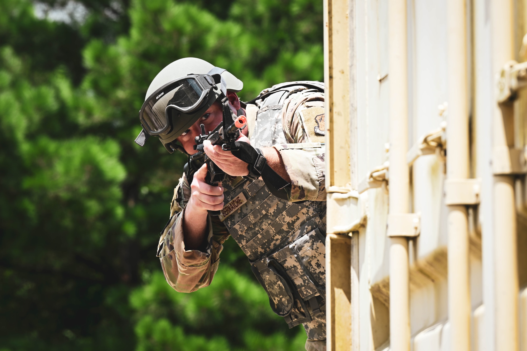 A man in uniform holding a gun peeks around a corner.