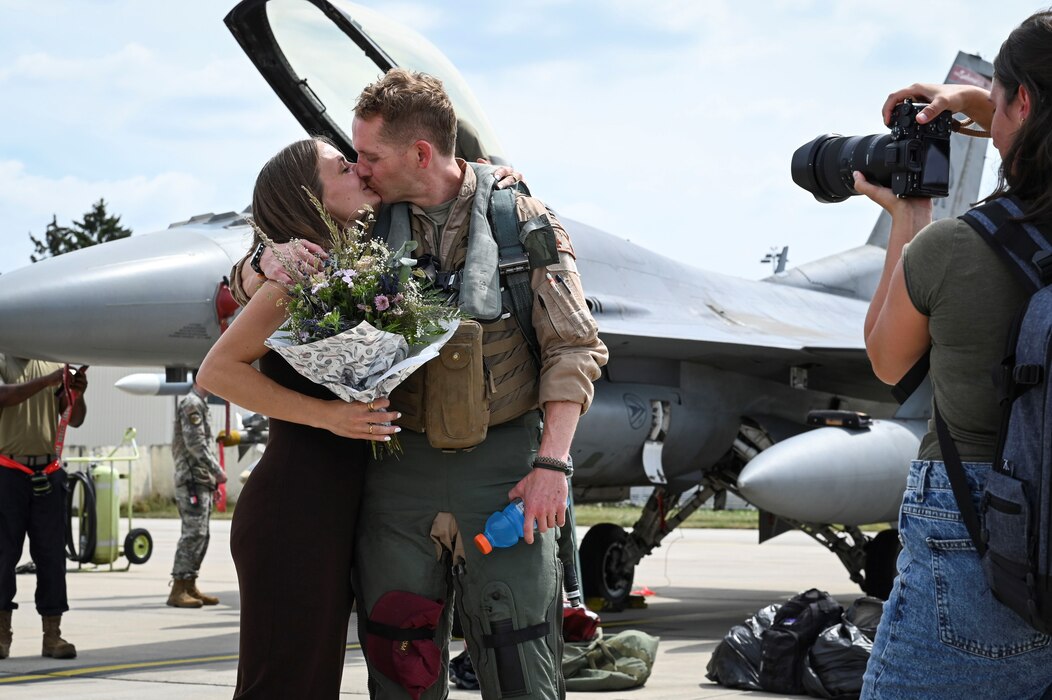 A woman photographs a U.S. Air Force pilot kissing a woman.