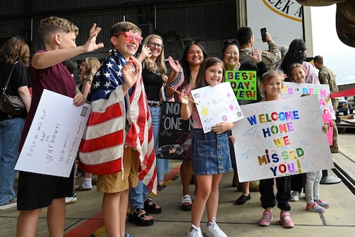 People in a crowd hold "Welcome home" signs.