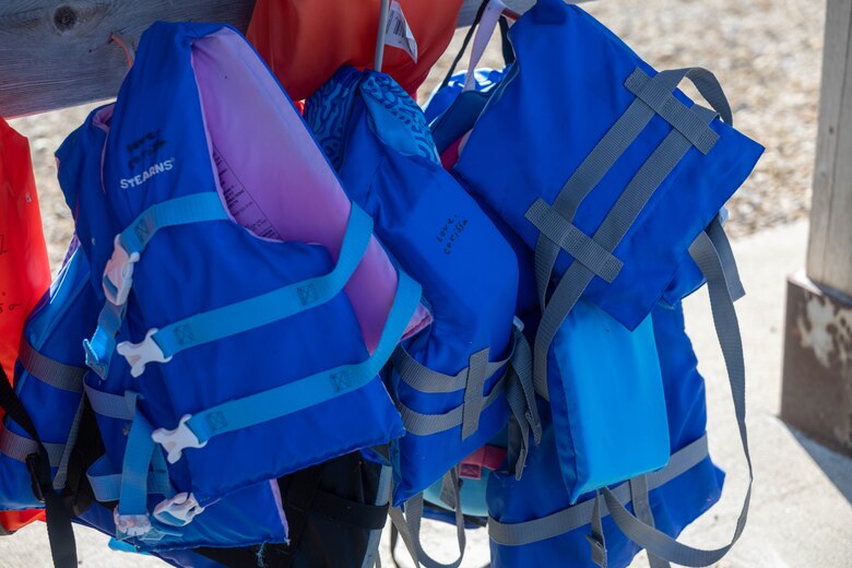 Blue lifejackets hang from hooks on a wooden board.