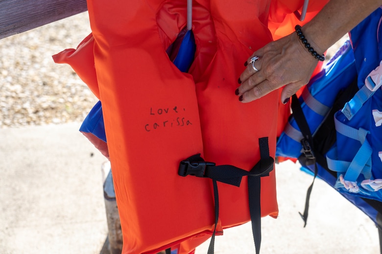 A woman's hand touches an orange lifejacket with a black strap and buckle.