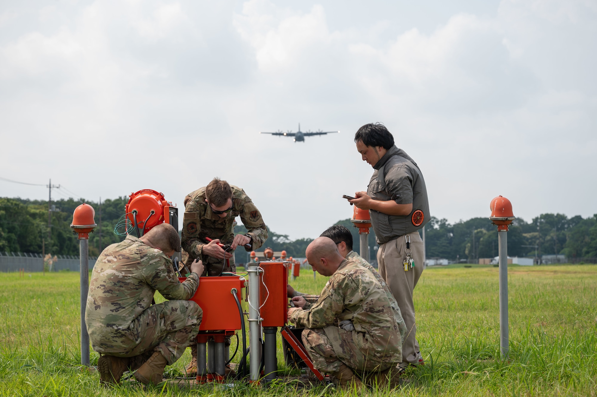 Airmen repair a light while an aircraft flies overhead.